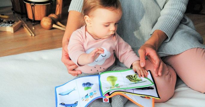 Bebê pequeno olha livro ao lado da mãe