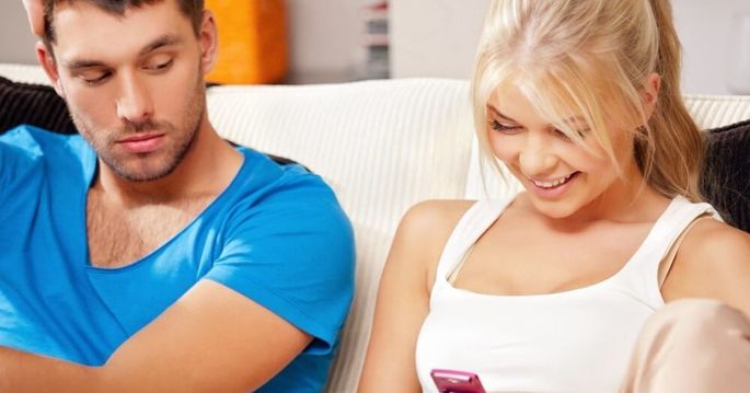 Namorada mexe em seu celular enquanto namorado olha com cara enciumada